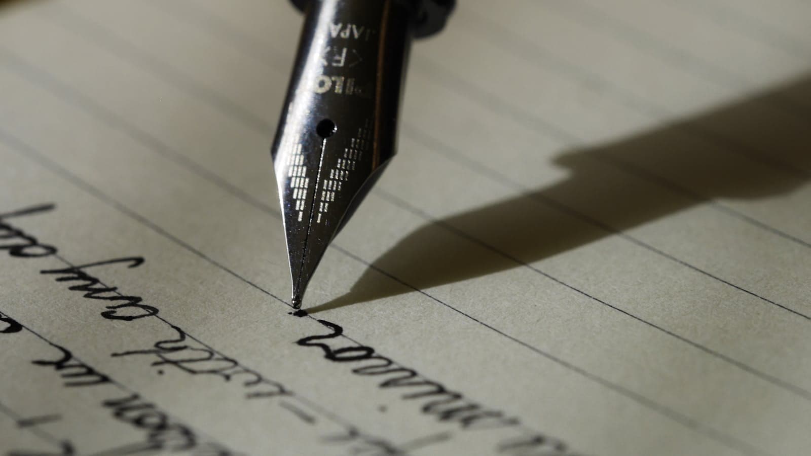 Close-up of a fountain pen nib writing in cursive on lined paper