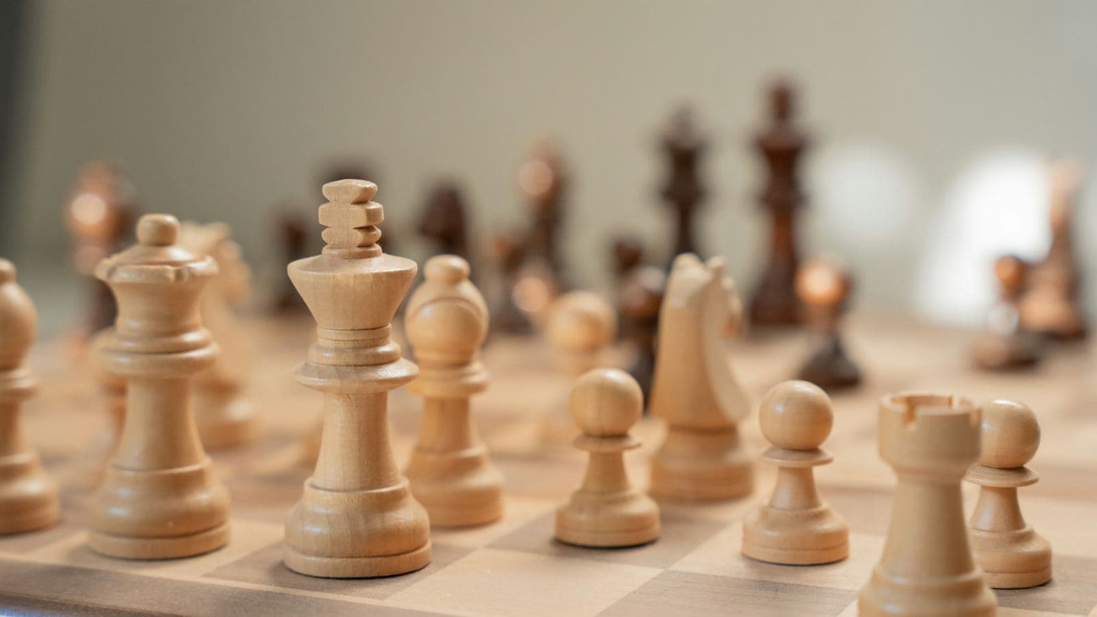 Close-up of wooden chess pieces on a board, with the king in focus and dark pieces blurred behind