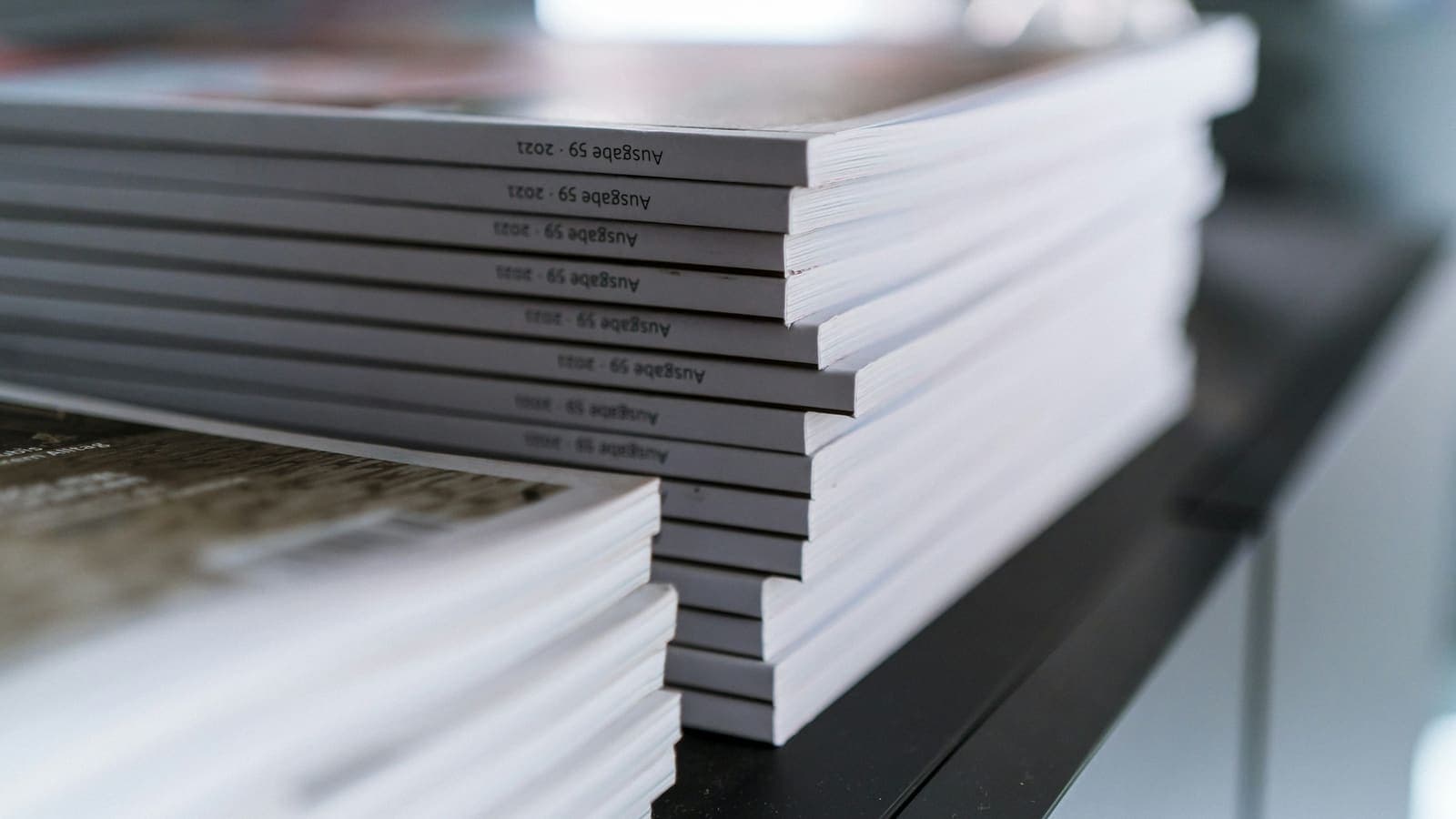 Close-up of two stacks of printed journal issues with white spines on a dark shelf