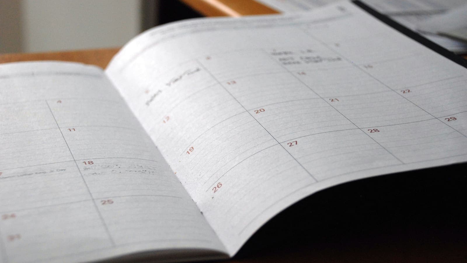 Open monthly planner lying on a wooden desk, its dated grid mostly empty apart from a few handwritten entries